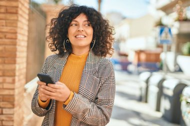 Genç İspanyol iş kadını şehirde akıllı telefon kullanarak mutlu gülümsüyor..
