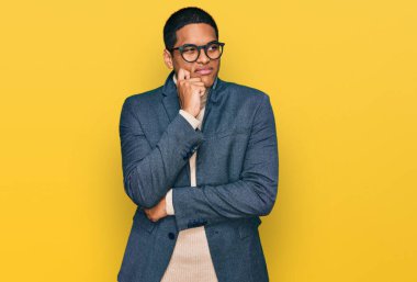 İş ceketi ve gözlük takan yakışıklı İspanyol bir adam ciddi bir yüzle eli çenesinde soru soran, kafa karıştırıcı bir fikir hakkında düşünceli. 