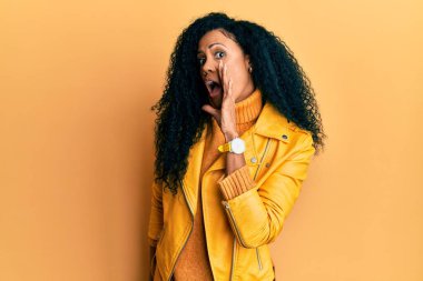 Orta yaşlı Afro-Amerikalı kadın yün kazak ve deri ceket giyiyor elleri ağızda gizli dedikodular anlatıyor, kötü niyetli konuşmalar fısıldıyor. 