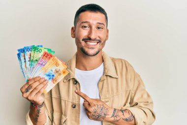 Dövmeleri olan yakışıklı bir adam İsviçre frangı banknotları tutuyor mutlu bir şekilde el ve parmak işareti yapıyor. 