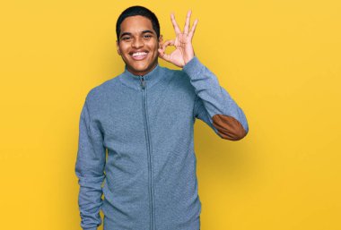 Gündelik kazak giyen genç, yakışıklı İspanyol adam gülümsüyor ve el ve parmaklarıyla 