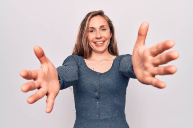 Genç, güzel, sarışın bir kadın izole edilmiş beyaz arka planda durup kameraya bakarak sarılmak için kollarını açmış gülümsüyor. Mutluluğu kucaklayan neşeli bir ifade.. 