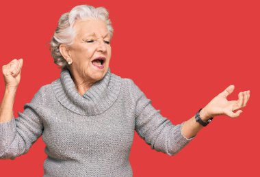 Kış süveteri giyen, mutlu ve neşeli dans eden, gülümseyen, rahat ve kendinden emin bir şekilde müzik dinleyen yaşlı, gri saçlı kadın. 