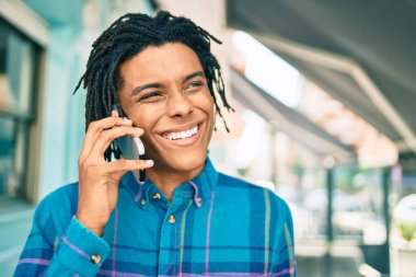 Genç Afrikalı Amerikalı gülümseyen mutlu bir adam şehrin caddesinde akıllı telefondan konuşuyor..
