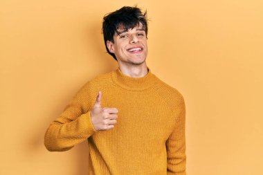 Yakışıklı hippi genç adam gündelik sarı süveter giyiyor mutlu bir el hareketi yapıyor. Kameraya bakıp başarıyı gösteren ifade. 