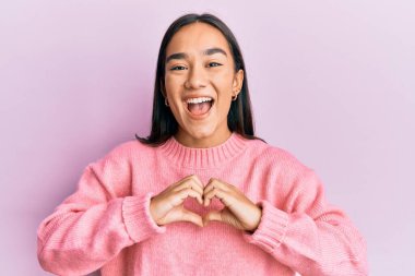Genç Asyalı kadın kalp sembolü yapıyor elleri ile gülüyor ve kahkahalarla gülüyor çünkü komik, çılgınca bir şaka.. 