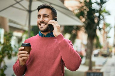 Genç İspanyol adam akıllı telefondan konuşuyor. Şehirde kahve içiyor..