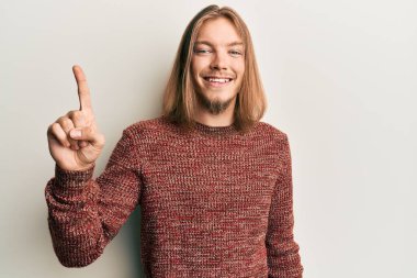 Uzun saçlı, sıradan bir kazak giyen yakışıklı beyaz bir adam bir fikir ya da soruyla gülümsüyor ve mutlu bir yüzle işaret ediyor. 