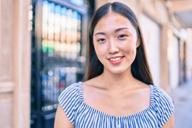 Genç Çinli kadın gülümsüyor. Şehrin caddesinde mutlu bir şekilde yürüyor..