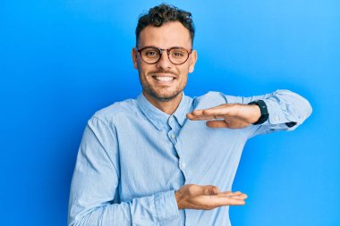 Gündelik kıyafetler giyen ve büyük boy ve ölçü işareti gösteren el kol hareketleri yapan Latin kökenli genç bir adam. Kameraya bakıp gülümsüyor. ölçüm kavramı. 