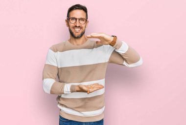 Sakallı, sıradan kıyafetler giyen ve elleri büyük ve büyük bir işaret gösteren gözlüklü yakışıklı bir adam. Ölçü sembolü. Kameraya bakıp gülümsüyor. ölçüm kavramı. 