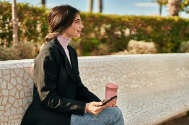 Genç ve güzel bir iş kadını kahve içiyor ve akıllı telefon kullanıyor..