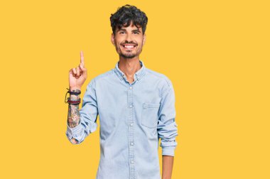 Gündelik kıyafetler giyen genç İspanyol bir numarayı gösterip işaret ederken kendinden emin ve mutlu bir şekilde gülümsüyor.. 