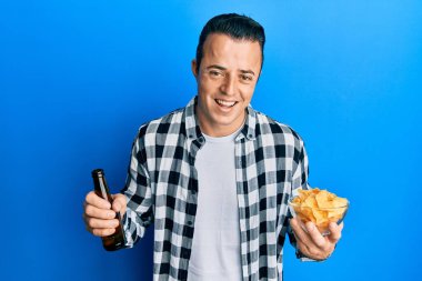 Yakışıklı genç adam bira içiyor elinde cipslerle gülüyor ve kahkahalarla gülüyor.. 