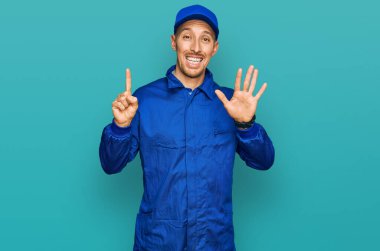 Sakallı, inşaatçı tulumu giyen kel bir adam altı numaralı parmaklarıyla kendini gösterip gülümserken mutlu ve kendinden emin.. 