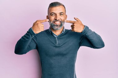 Orta yaşlı, sıradan kıyafetler giyen, neşeli gülümseyen, parmaklarıyla ve ağzıyla işaret eden yakışıklı bir adam. diş sağlığı kavramı. 