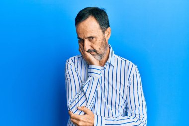 Orta yaşlı İspanyol bir adam gündelik kıyafetler giyip kollarını kavuşturarak depresyondan sıkılmış ve yorgun görünüyor.. 