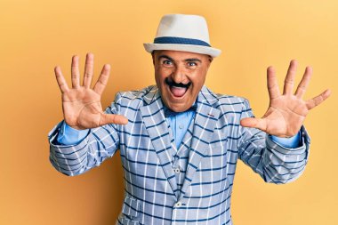 Olgun, orta doğulu bıyıklı, klasik ve şık moda tarzlı bir adam on numaralı parmaklarıyla onu gösterirken kendinden emin ve mutlu gülümsüyor.. 