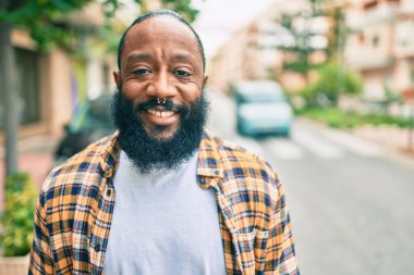 Sakallı, yakışıklı, Afro-Amerikan adam. Sokakta durup gülümsüyor.