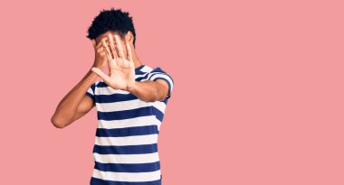 Genç, Afro-Amerikan bir adam, günlük kıyafetler giyiyor, elleriyle gözleri örtüyor ve üzgün ve korku ifadeleriyle jestleri durduruyor. utangaç ve olumsuz kavram. 