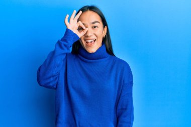 Genç Asyalı kadın, sıradan bir kazak giyiyor. El hareketleriyle gülümsüyor ve mutlu yüzüyle parmaklarının arasından bakıyor.. 