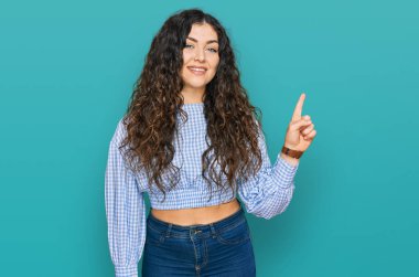 Yüzünde kocaman bir gülümseme olan, gündelik kıyafetler giyen genç İspanyol kız, kameraya el ile işaret ediyor.. 