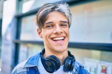 Genç İspanyol adam şehirde yürürken kulaklık takarak mutlu bir şekilde gülümsüyor..