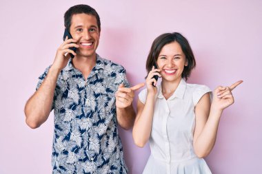 Akıllı telefondan konuşan güzel bir çift mutlu bir şekilde el ve parmak kenarı işaret ediyor. 