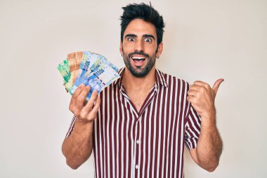 Yakışıklı, sakallı, Güney Afrika rand banknotları tutan, ağzı açık gülümseyen bir İspanyol. 