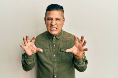 Gündelik kıyafetler giyen genç latin adam komik gülüyor kedi gibi pençe hareketi yapıyor, agresif ve seksi bir ifade. 