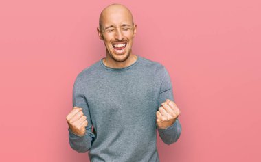 Kel, sakallı, günlük kıyafetler giyen, mutlu ve heyecanlı bir şekilde kolları havada, gülümseyen ve başarı için bağıran kazanan bir jest yapıyor. kutlama konsepti. 