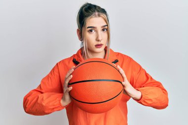 Young modern girl holding basketball ball relaxed with serious expression on face. simple and natural looking at the camera.  clipart