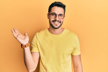 Gündelik kıyafetler ve gözlük takan genç İspanyol adam mutlu bir şekilde gülümsüyor ve avuç içi kameraya bakıyor.. 