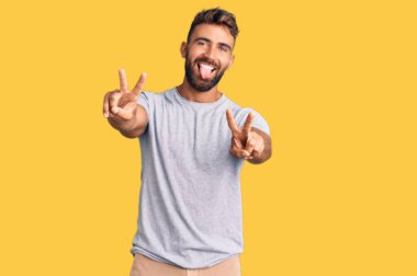 Gündelik giysiler giymiş, ağzı açık gülümseyen genç İspanyol adam zafer işareti yaparken parmaklarını gösteriyor. İki numara.. 