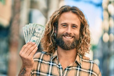 Beyaz bir adam gülümsüyor, şehirde dolarları elinde tutuyor..