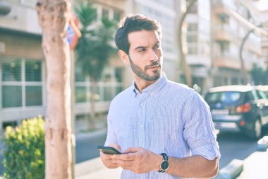 Şehirde akıllı telefon kullanan ciddi bir suratı olan genç bir İspanyol..