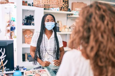 Giyim mağazasında çalışan, tıbbi maske takan Afro-Amerikan bir kadın.
