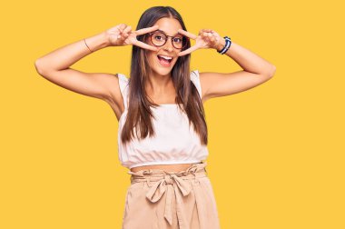 Gündelik kıyafetler ve gözlük takan genç İspanyol kadın barış sembolü yapıyor. Yüzünde parmaklar, gülümseyerek zaferi gösteriyor. 