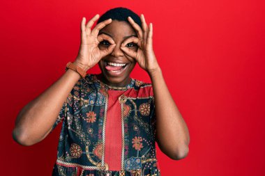 Afro-Amerikan tarzı giyinen Afro-Amerikan genç bir kadın dürbün gibi güzel hareketler yapıyor. Dürbün gibi dilini çıkarıyor, gözler parmaklarından bakıyor. çılgın ifade. 