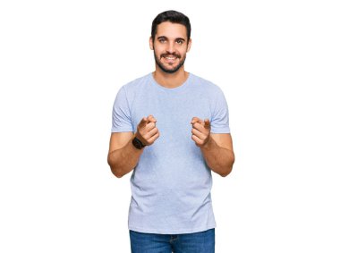 Günlük kıyafetler giyen genç İspanyol adam mutlu ve komik yüzüyle kamerayı işaret ediyor. iyi enerji ve titreşimler. 