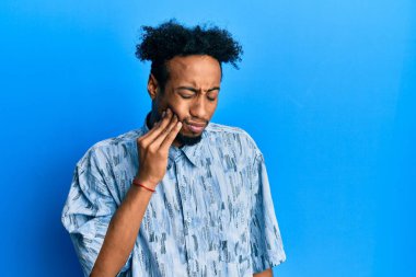 Young african american man with beard wearing casual clothes touching mouth with hand with painful expression because of toothache or dental illness on teeth. dentist 