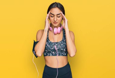 Güzel esmer kadın spor kıyafetleri giyiyor ve stres yüzünden baş ağrısı için kulaklık kullanıyor. migren ağrısı. 