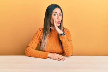 Latin kökenli genç bir kadın, gündelik giysiler içinde masanın üzerine oturmuş, ağzının üstüne oturmuş gizli dedikodular anlatıyor, kötü niyetli konuşmalar fısıldıyor. 