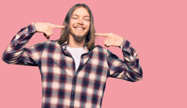 Handsome caucasian man with long hair wearing hipster shirt smiling cheerful showing and pointing with fingers teeth and mouth. dental health concept. 