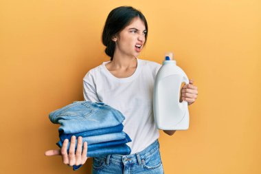Çamaşır deterjanı şişesiyle çamaşır yıkayan genç, beyaz bir kadın ve katlanmış kot pantolon sinirli, sinirli, öfkeli ve öfkeliydi. Öfkeyle bağırıyordu. öfke ve agresif konsept. 