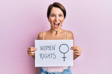 Kısa saçlı esmer kadın kadın kadın kadın hakları pankartı tutuyor. Çılgınlığı kutluyor ve başarı için hayrete düşüyor. Gözleri açık, heyecanlı çığlıklar atıyor.. 