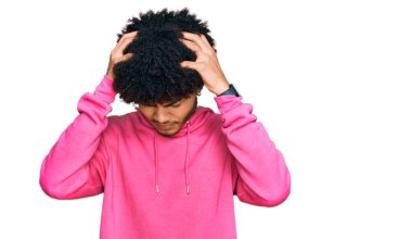 Afro saçlı, başı ağrıyan ve migren ağrısı çeken sıradan pembe kazaklar giyen Afro-Amerikalı genç bir adam. Eller başının üstünde.. 