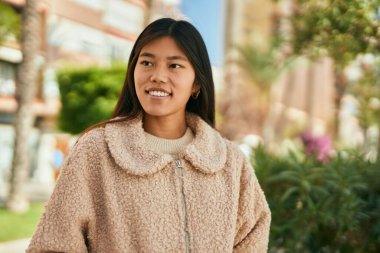 Genç Asyalı kadın şehirde mutlu bir şekilde ayakta gülümsüyor..