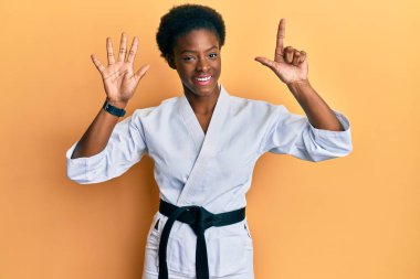 Genç Afro-Amerikalı kız karate kimonosu ve siyah kuşak takıyor ve yedinci parmaklarını gösterirken kendinden emin ve mutlu gülümsüyor.. 