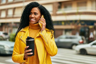 Orta yaşlı Afro-Amerikalı kadın akıllı telefondan konuşuyor ve şehirde kahve içiyor..